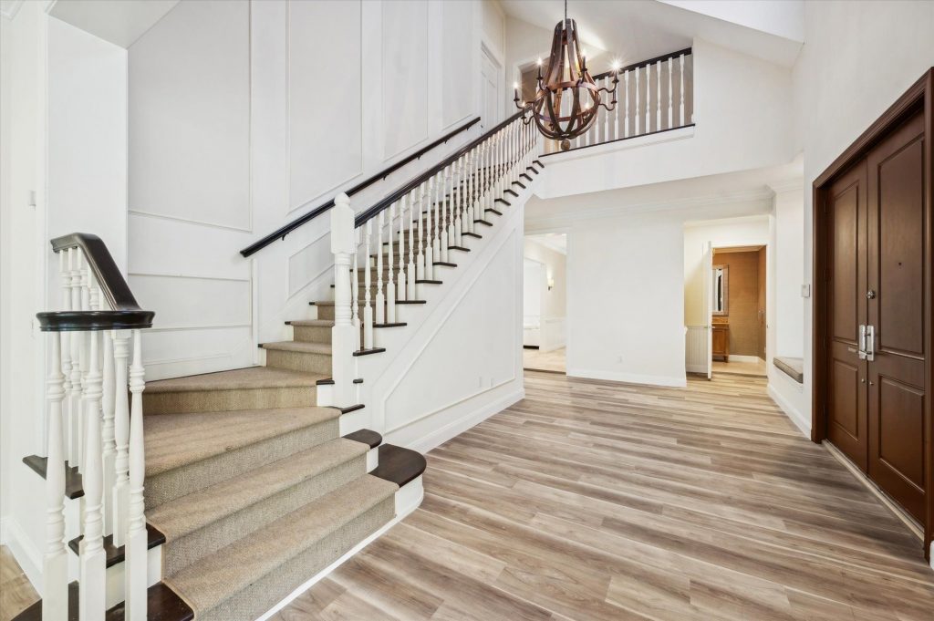 Grand two-story foyer with carpeted staircase, light hardwood floors and rustic wood chandelier